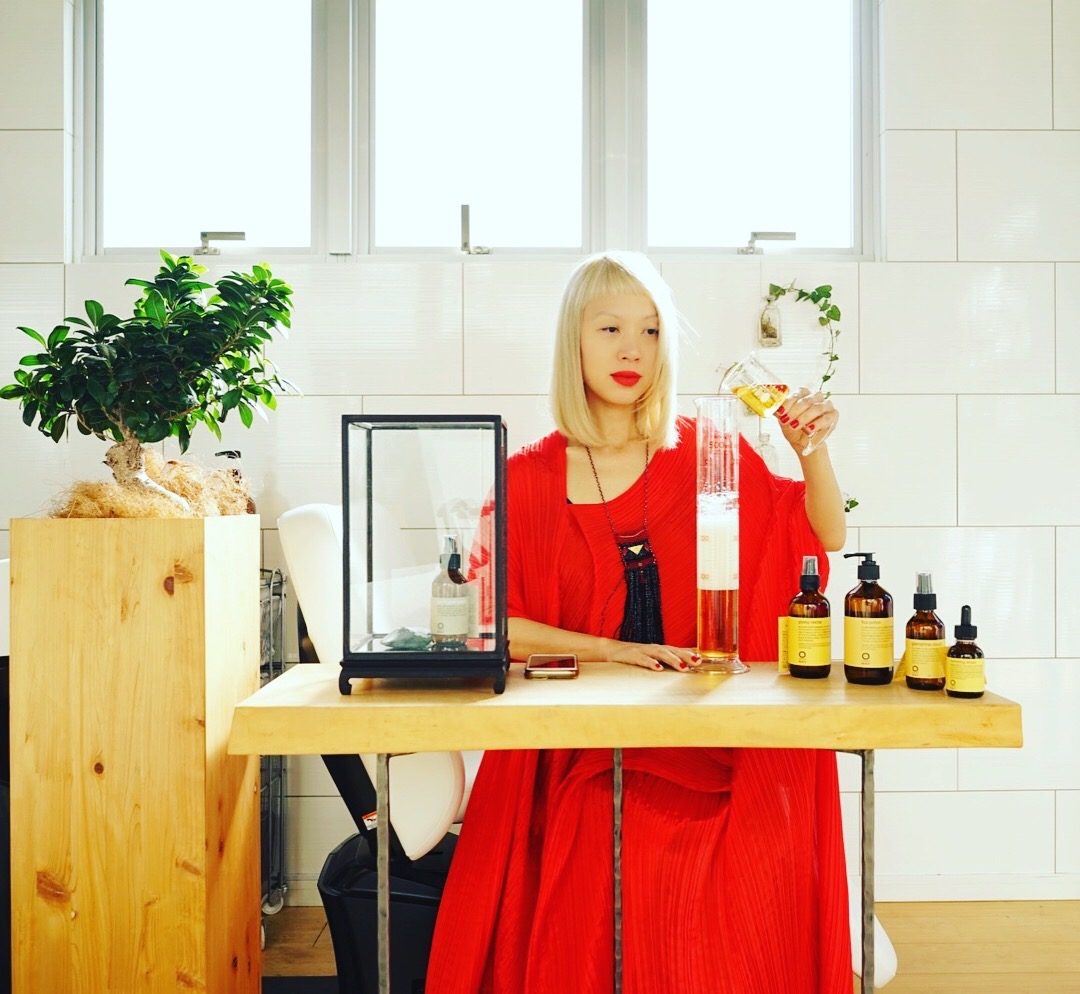 Marianne en rouge au salon, versant un soin dans une éprouvette, les flacons OWAY alignés sur la table.